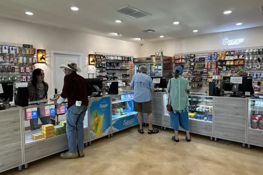 Nature’s Wonder Cave Creek Dispensary Staff Assistance Staff at Nature’s Wonder Cave Creek Dispensary assisting customers at a counter with a display of cannabis products, surrounded by plants and shelves.