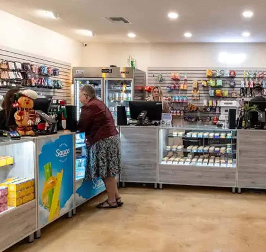 A customer at the counter of Nature's Wonder Cave Creek Dispensary A customer at the counter of Nature's Wonder Cave Creek Dispensary, with a decorated figurine, staff assisting, and shelves stocked with various products.